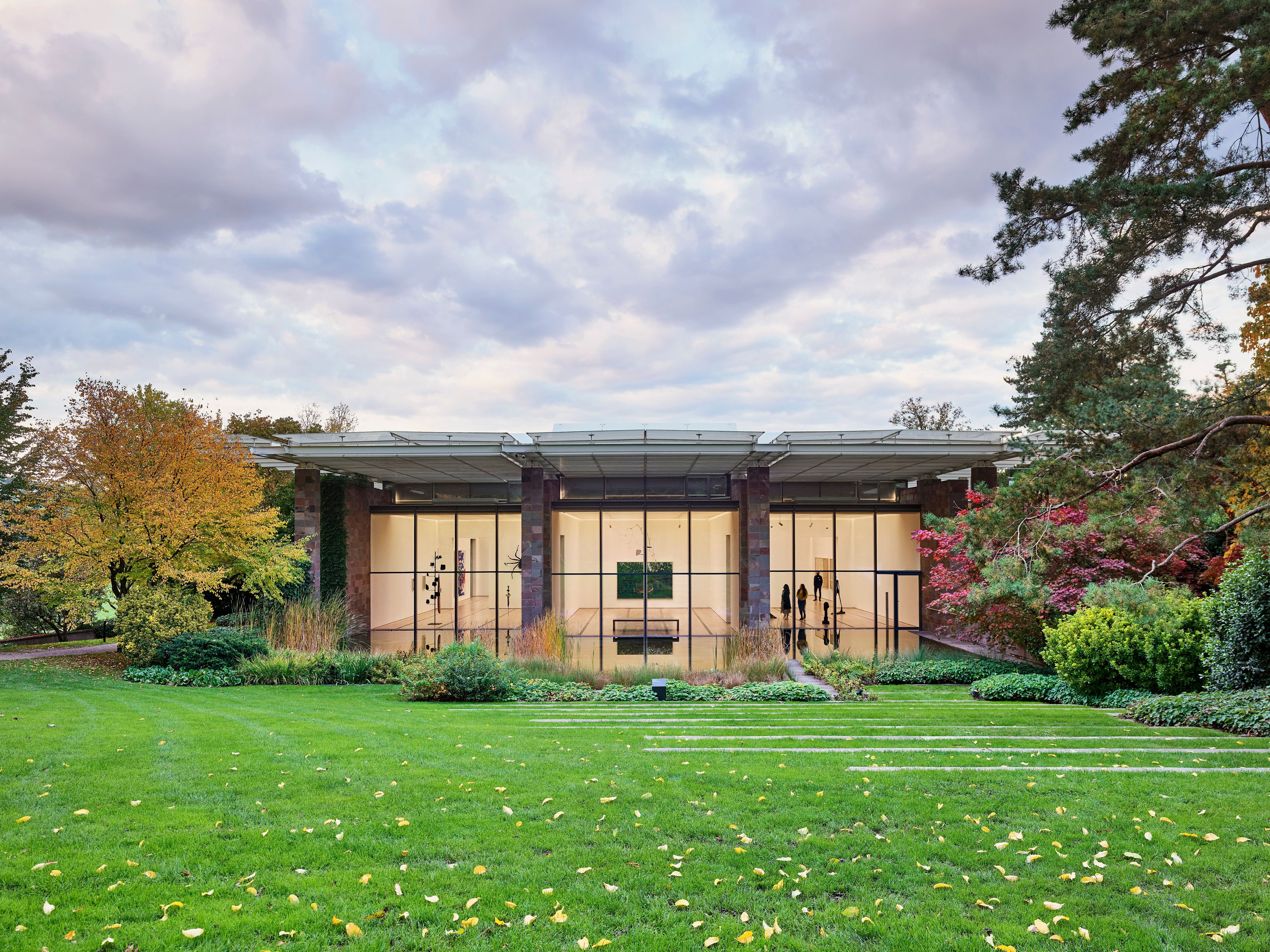 Vue de face du musée avec pelouse verte, arbres et ciel nuageux. Musées et nature.